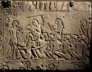 A group of Black prisoners surrounded by guards armed with clubs while a scribe draws up a report, relief from the tomb of Horemheb at Saqqara