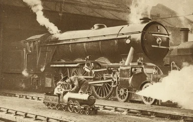 Boy riding a toy steam locomotive in front of the real thing