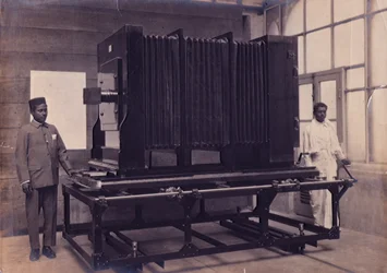 Two Indian assistants standing beside the massive camera in the Photographic Department of the Survey of India, c.1911