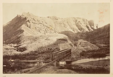 Views on the Pacific Railway, of railway track crossing a river on a girder bridge, with mountains beyond