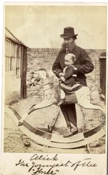 Young girl on a rocking horse in the garden, her father beside