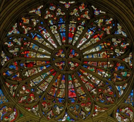 Window w217, the north rose window, depicting the Coronation of the Virgin in the two uppermost openings, surrounded by angels carrying musical instruments and the Instruments of the Passion (rose window)