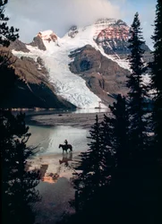 Lone horse and rider reflect on lake at base of Canada