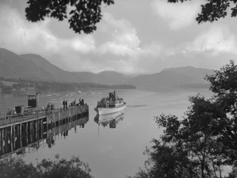 A boat carrying people on a lake nearing a jetty, hills in background