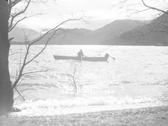 A man fishing in a boat on a lake, hills in background