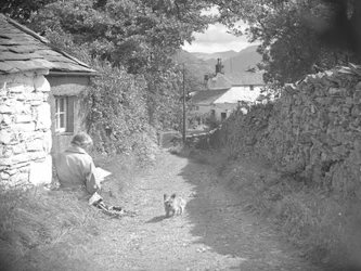 A woman sat reading with a dog in a lane