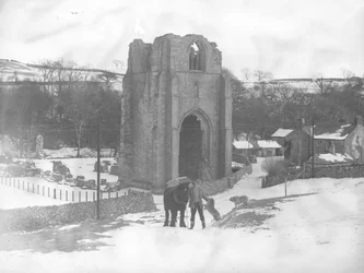 Man with horse and two dogs in front of Shap Abbey remains in the snow