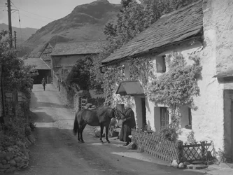 Old lady stroking horse standing in the road in front of cottage