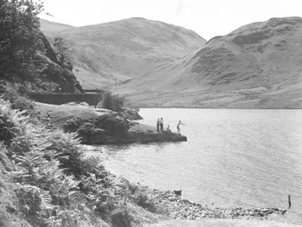 Three men and a woman on a rocky outcrop in the lake fishing, fells in background