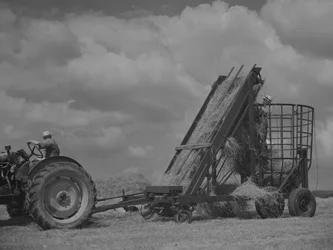 Tractor pulling mobile frame and hay being loaded into it