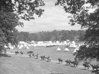 View of multiple cone-shaped tents, men in uniform on horseback (army?)