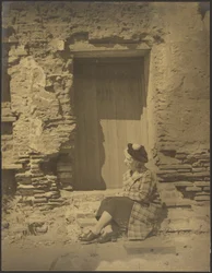 Woman Seated Before Deteriorating Building