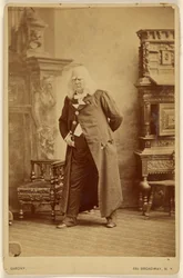 [Actor in long white wig with white bushy eyebrows, standing]