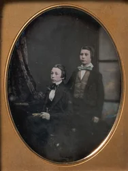 Two Young Men in Bow Ties, One Seated Holding a Book, One Standing