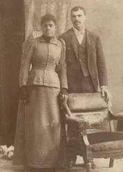 Photograph of an African-American couple standing behind a chair