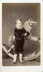 Young Boy Standing by a Rocking Horse