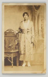 Photographic Postcard of a Woman Standing Next to a Wooden Chair, 1904-1918