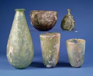 Clockwise from left: pear-shaped green glass flask, Sasanian, 3rd-7th century AD; pale amber glass bowl, Sasanian, 5th-6th century AD; Islamic green glass pear-shaped flask, c.8th-12th century AD; two Islamic green glass beakers, c.9th century AD