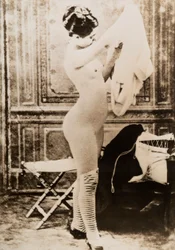 Full-length nude portrait of a young woman dressing