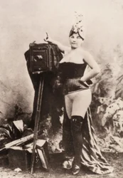 Portrait of a partially nude woman leaning on an antique camera