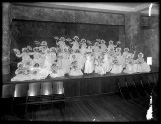 Group of little girls posed on a small stage holding fans, probably the Roman Catholic Orphan Asylum, Kingsbridge, Bronx, c.1911